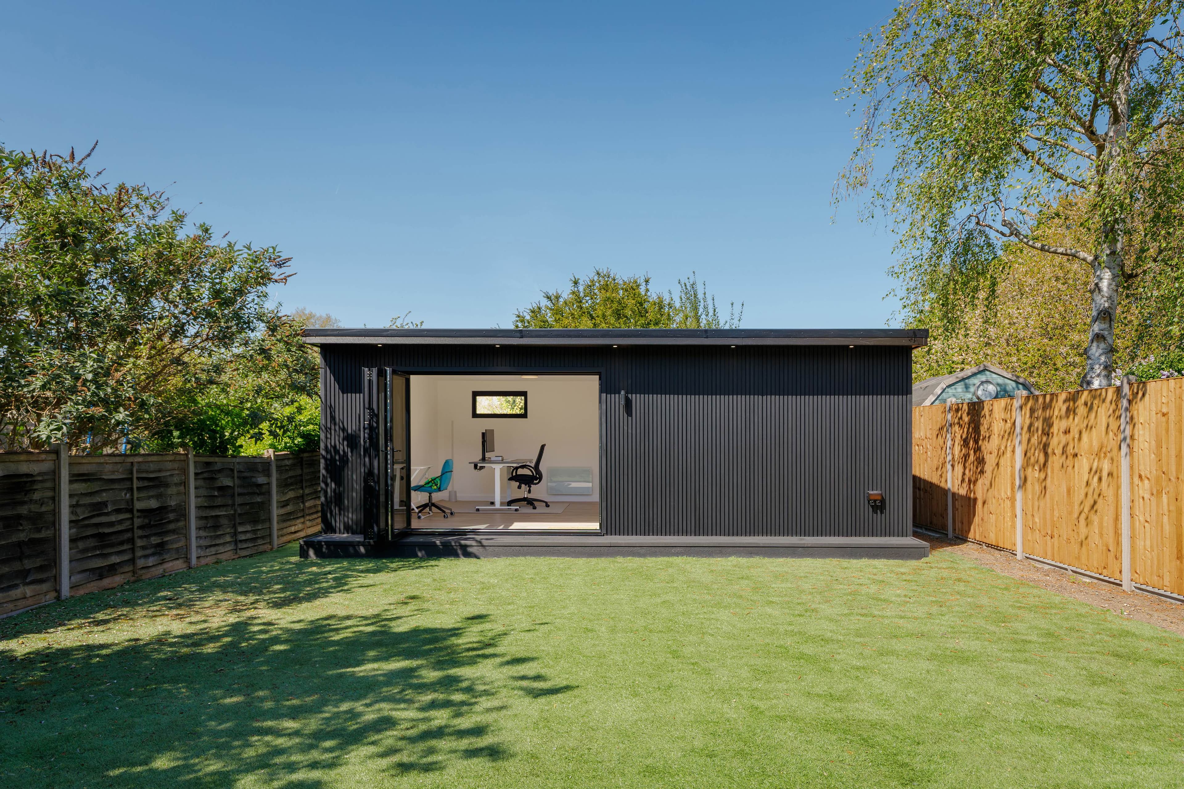 Anthracite-clad garden office in Bedfordshire with bifold doors open to a desk setup, seen across a sunny lawn