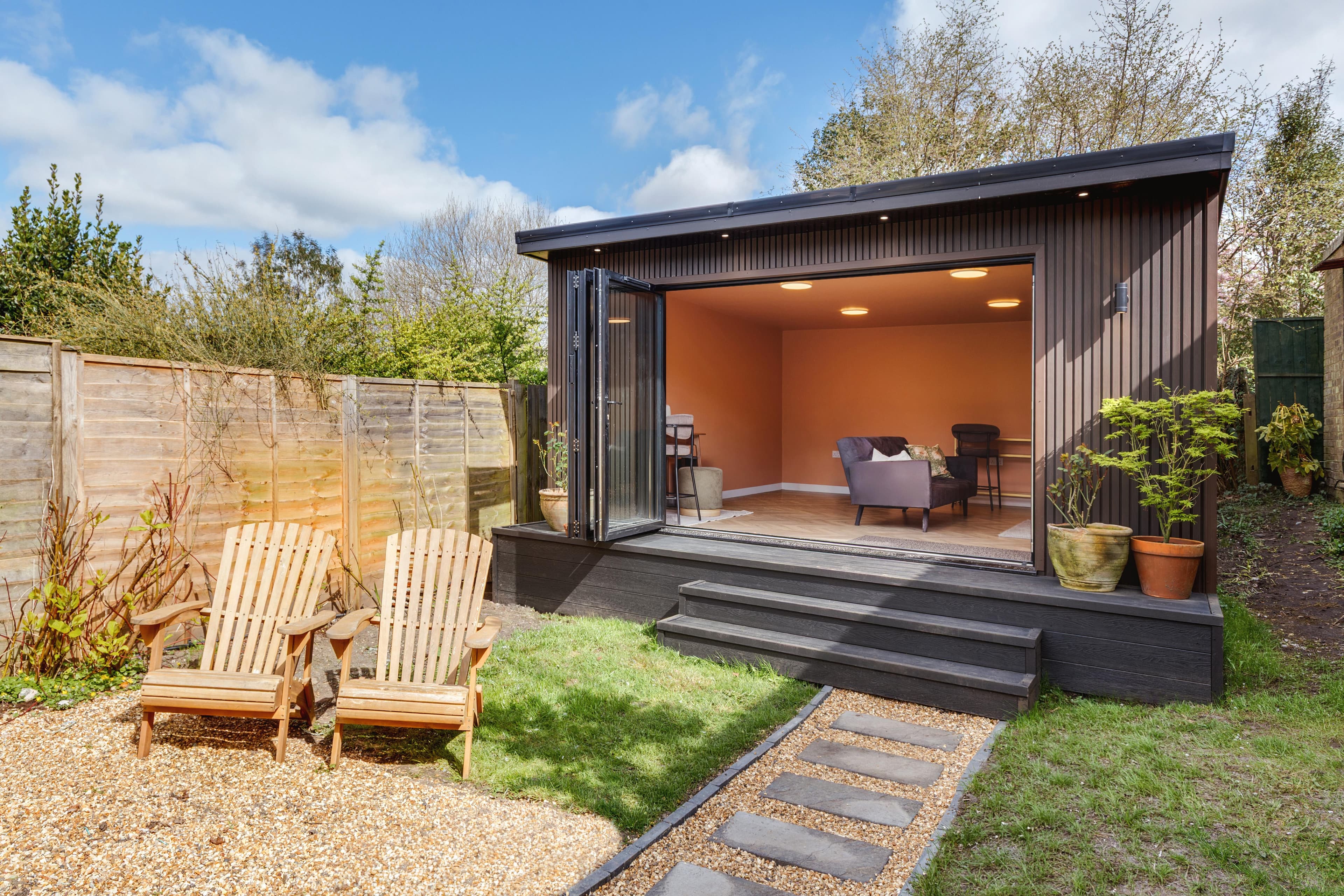Black-clad garden room in Bedfordshire with a terracotta interior and a stepping-stone path across the lawn
