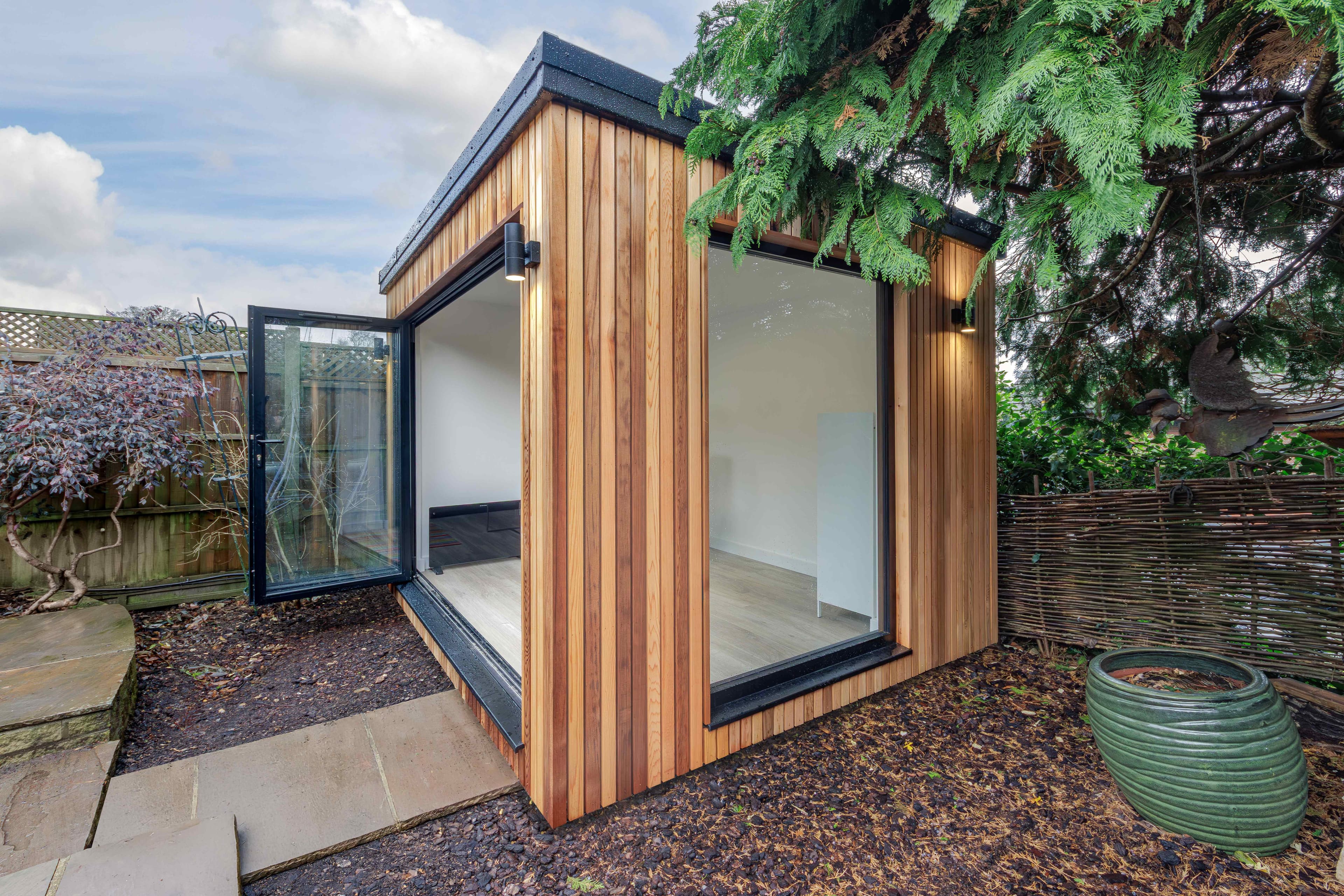 Cedar-clad corner garden studio in Bedfordshire with a large picture window and a single door open to the garden