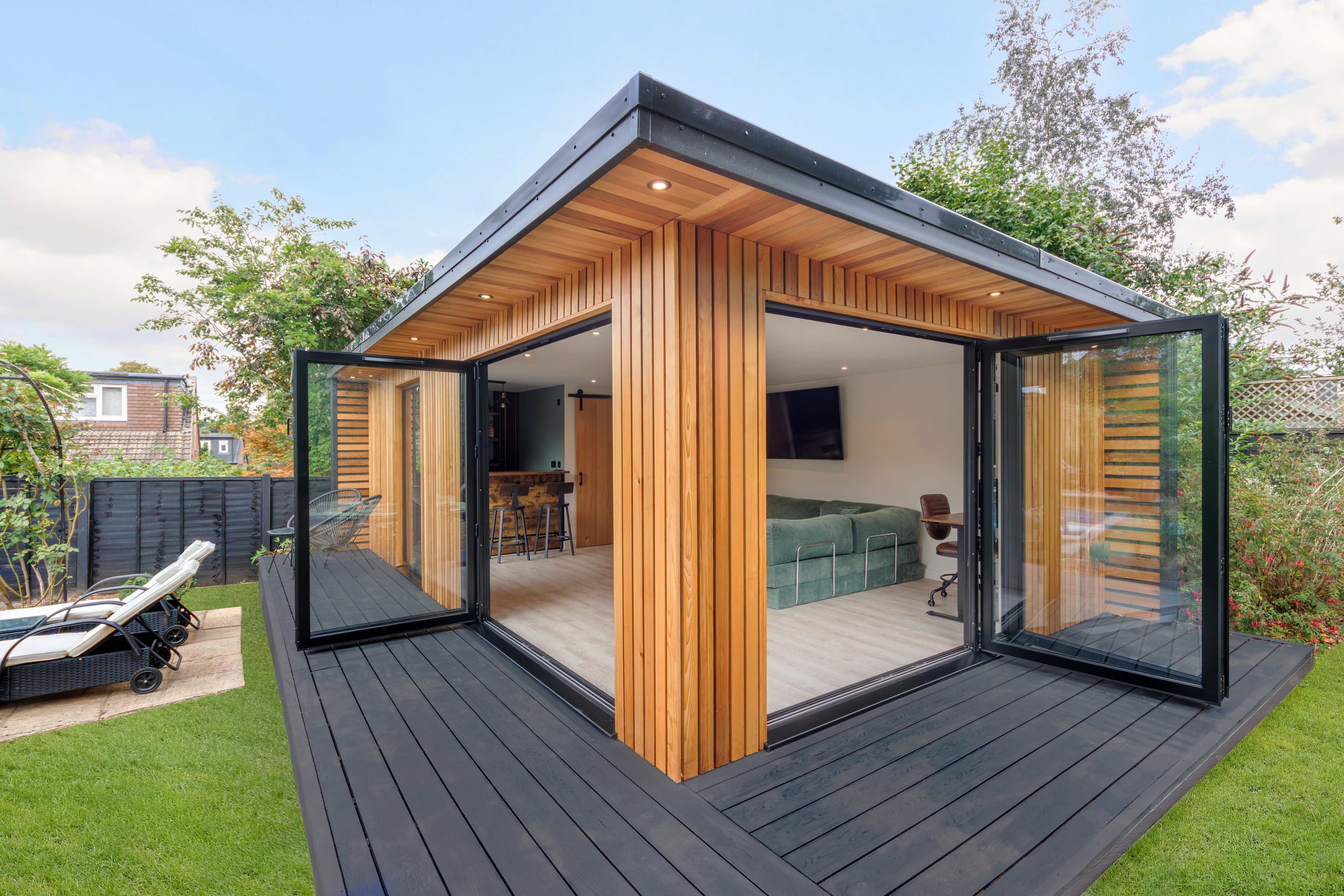 Cedar-clad garden room in Bedfordshire with corner bifold doors open to a lounge and bar area, set on black decking