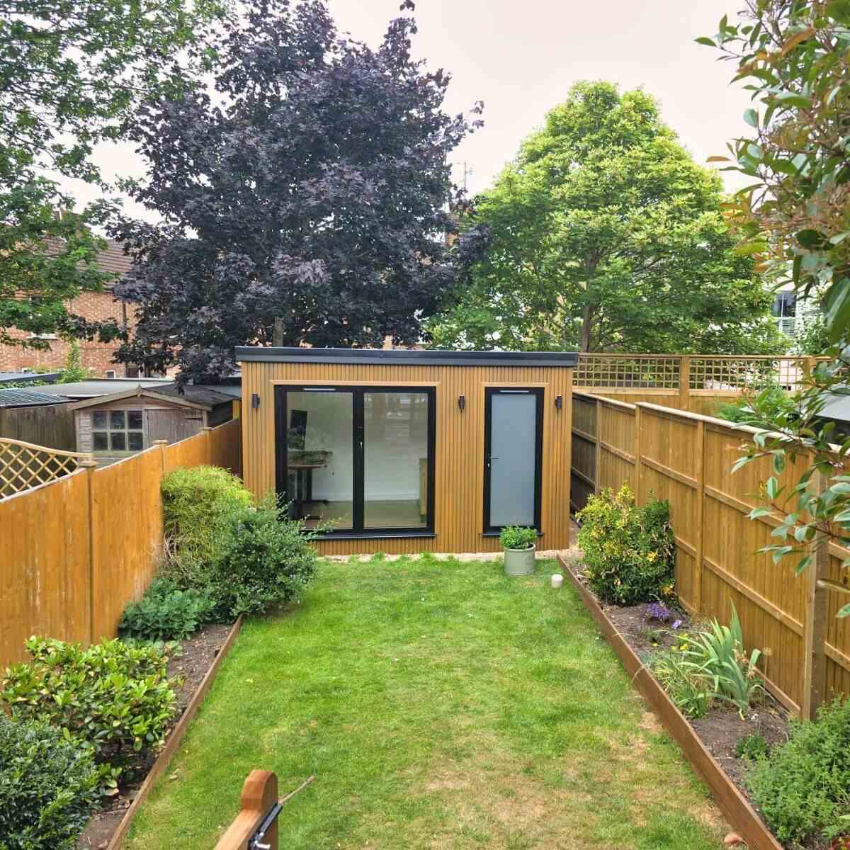Cedar-clad garden room in Bedfordshire at the end of a narrow lawned garden with planted borders