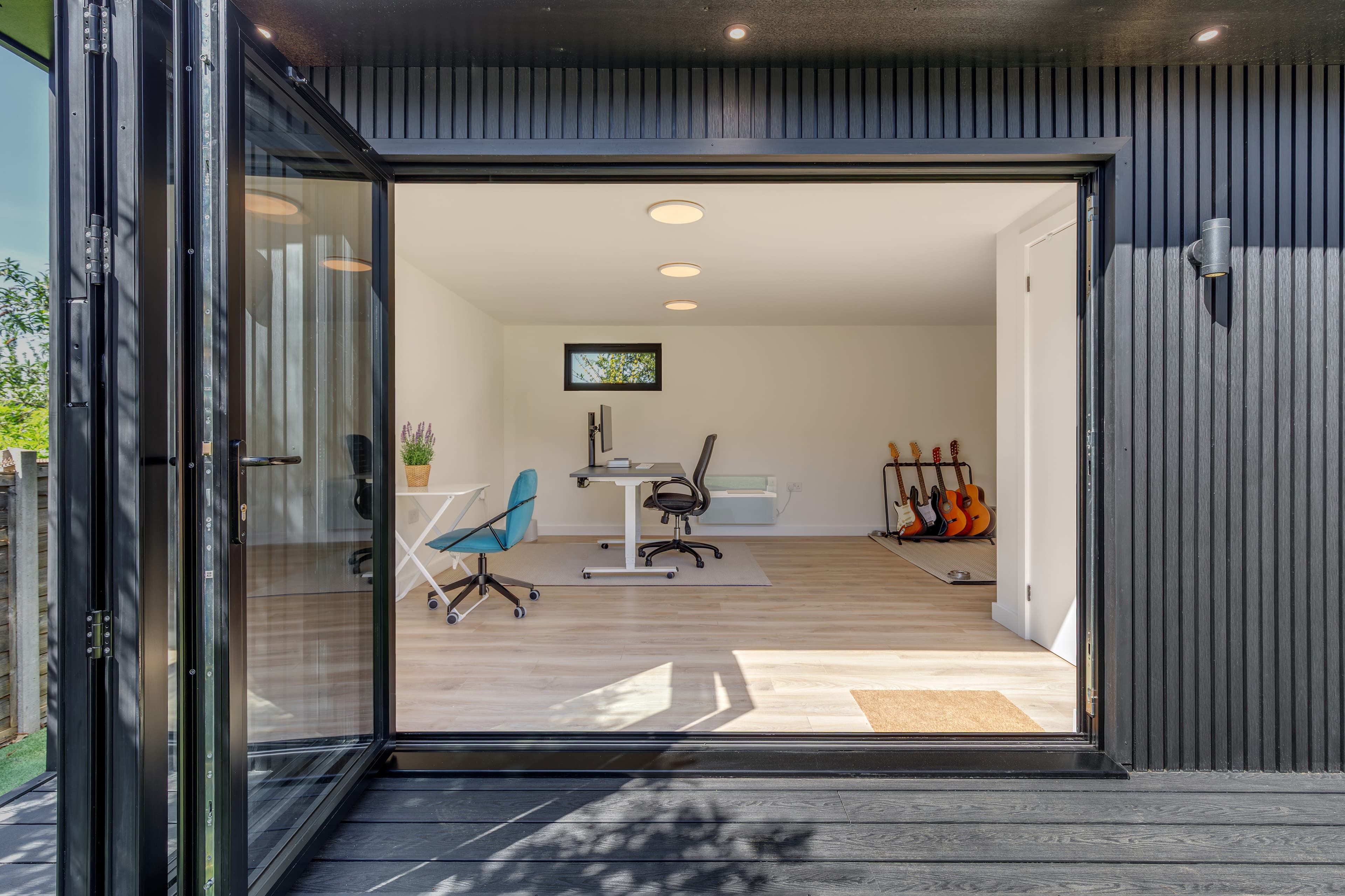 Dark-clad garden office and music room in Bedfordshire with sliding doors open to a desk and instruments inside
