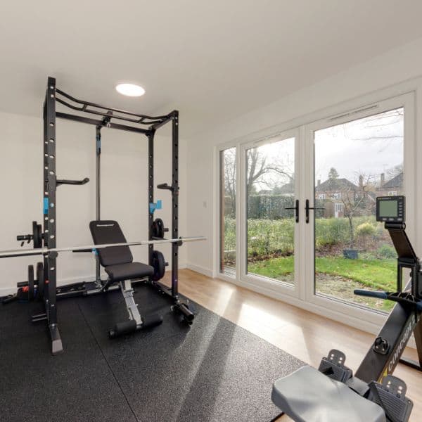 Garden gym in Bedfordshire fitted with a power rack, weight bench and rowing machine beside French doors