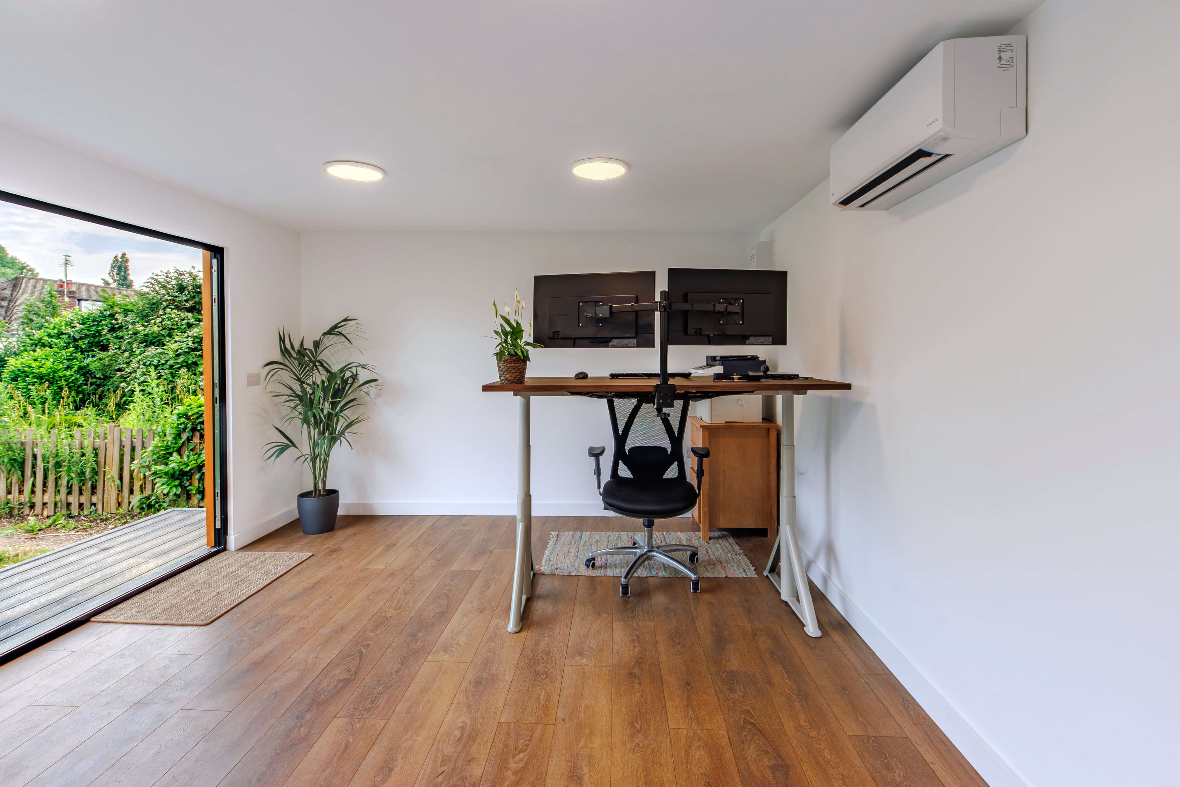 Garden office interior in Bedfordshire with a standing desk, dual monitors and a wall-mounted air conditioning unit