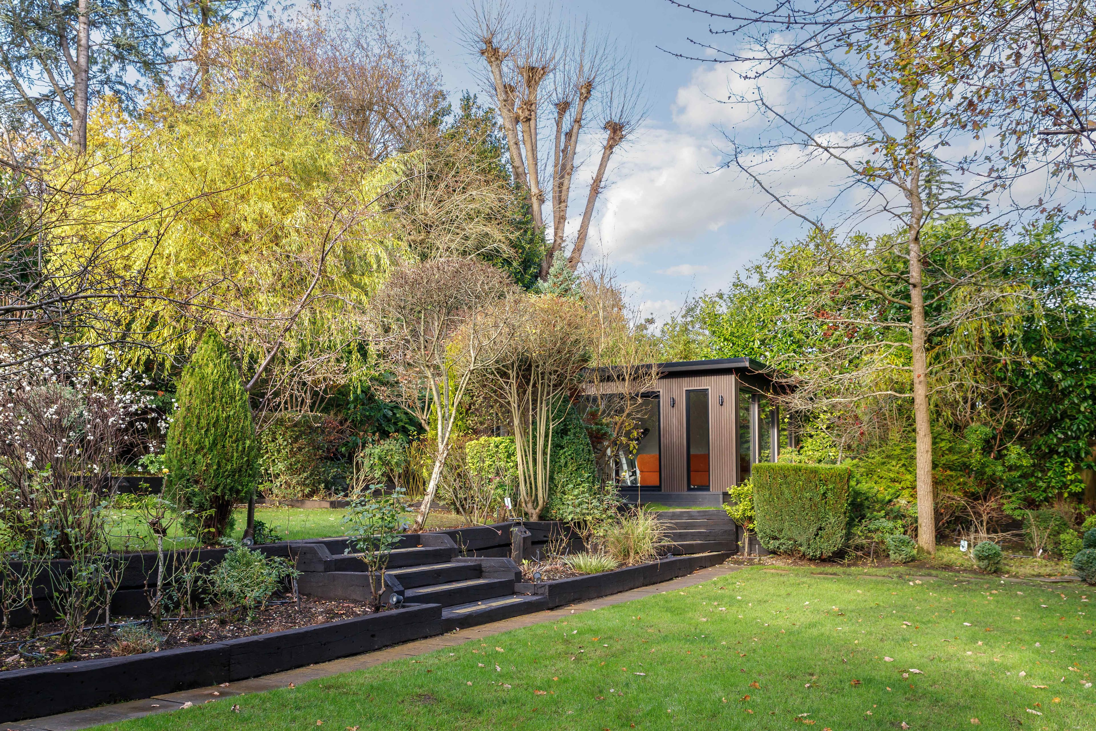 Garden room in Bedfordshire nestled among autumn planting with railway-sleeper steps leading up to it