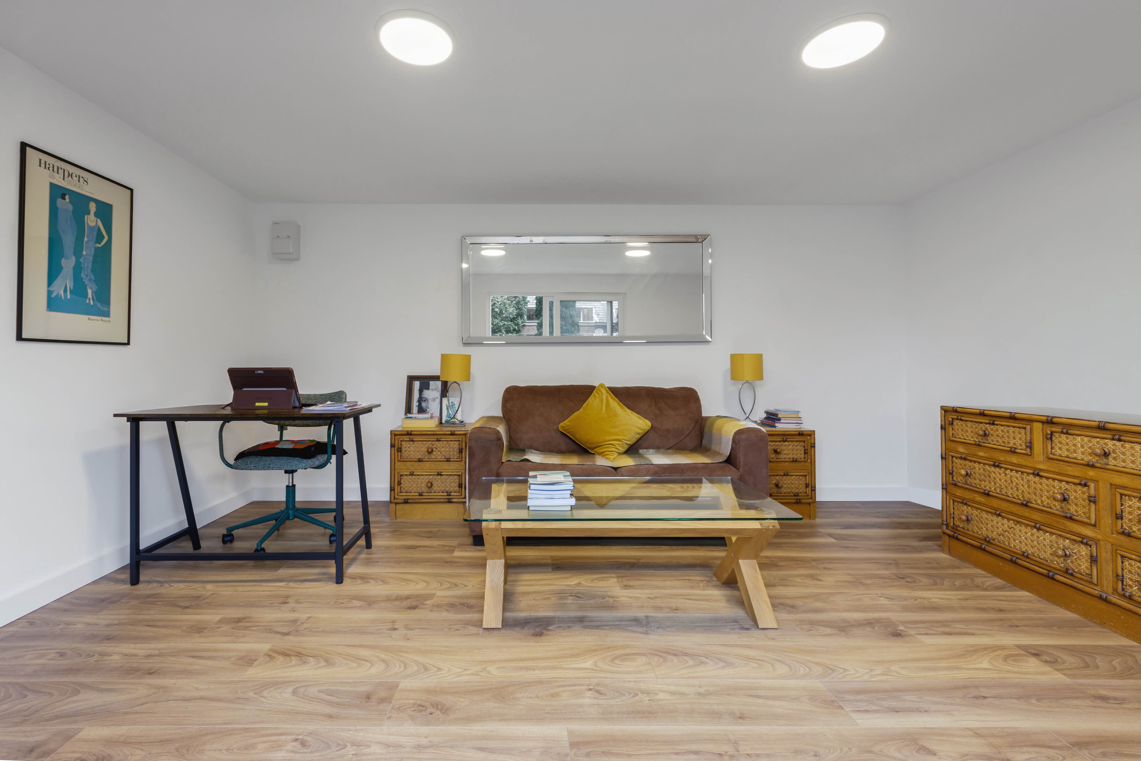 Garden room lounge in Bedfordshire with a brown sofa, mustard cushion, desk and framed print on white walls
