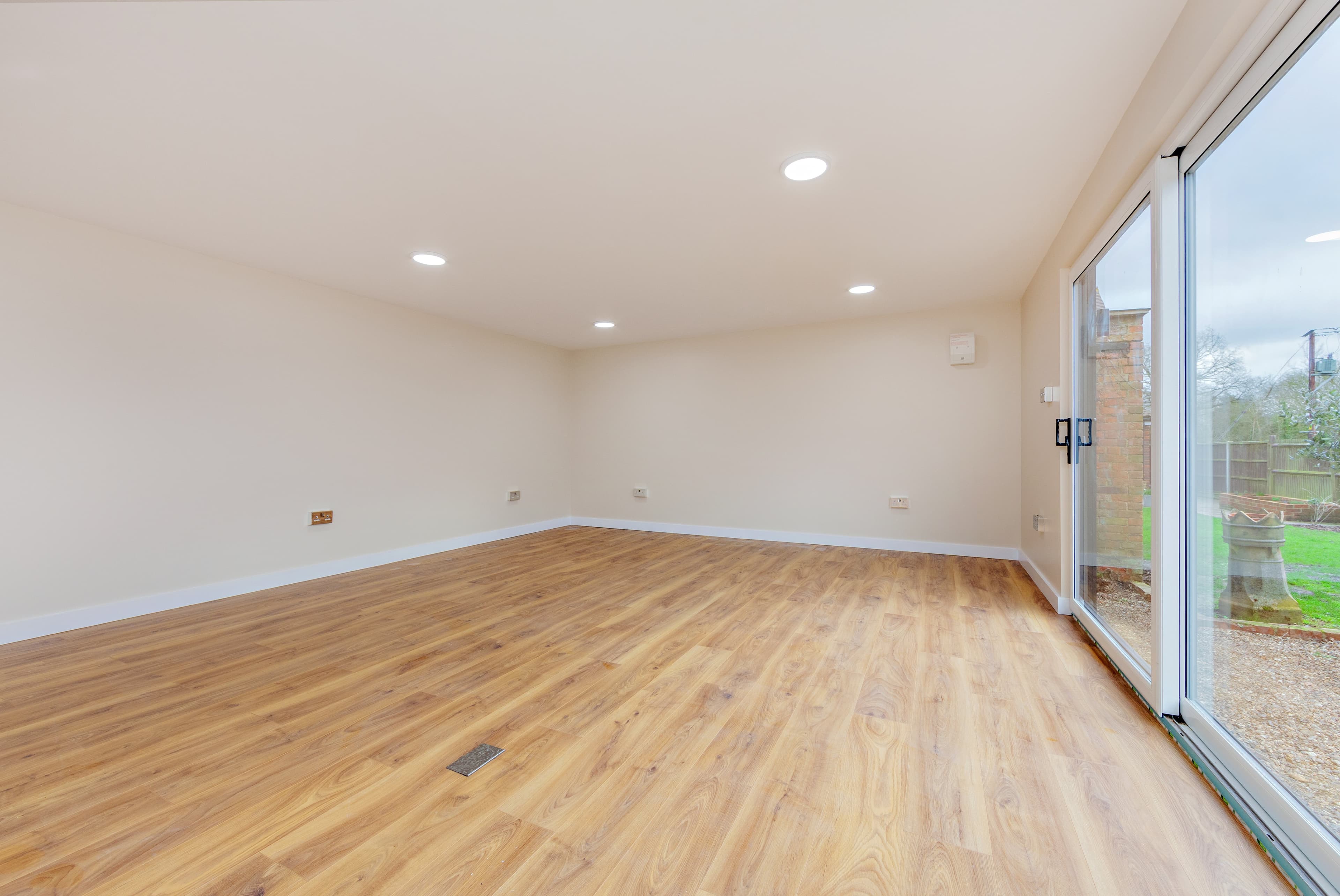 Garden room interior in Bedfordshire with light oak flooring and white sliding doors onto the lawn