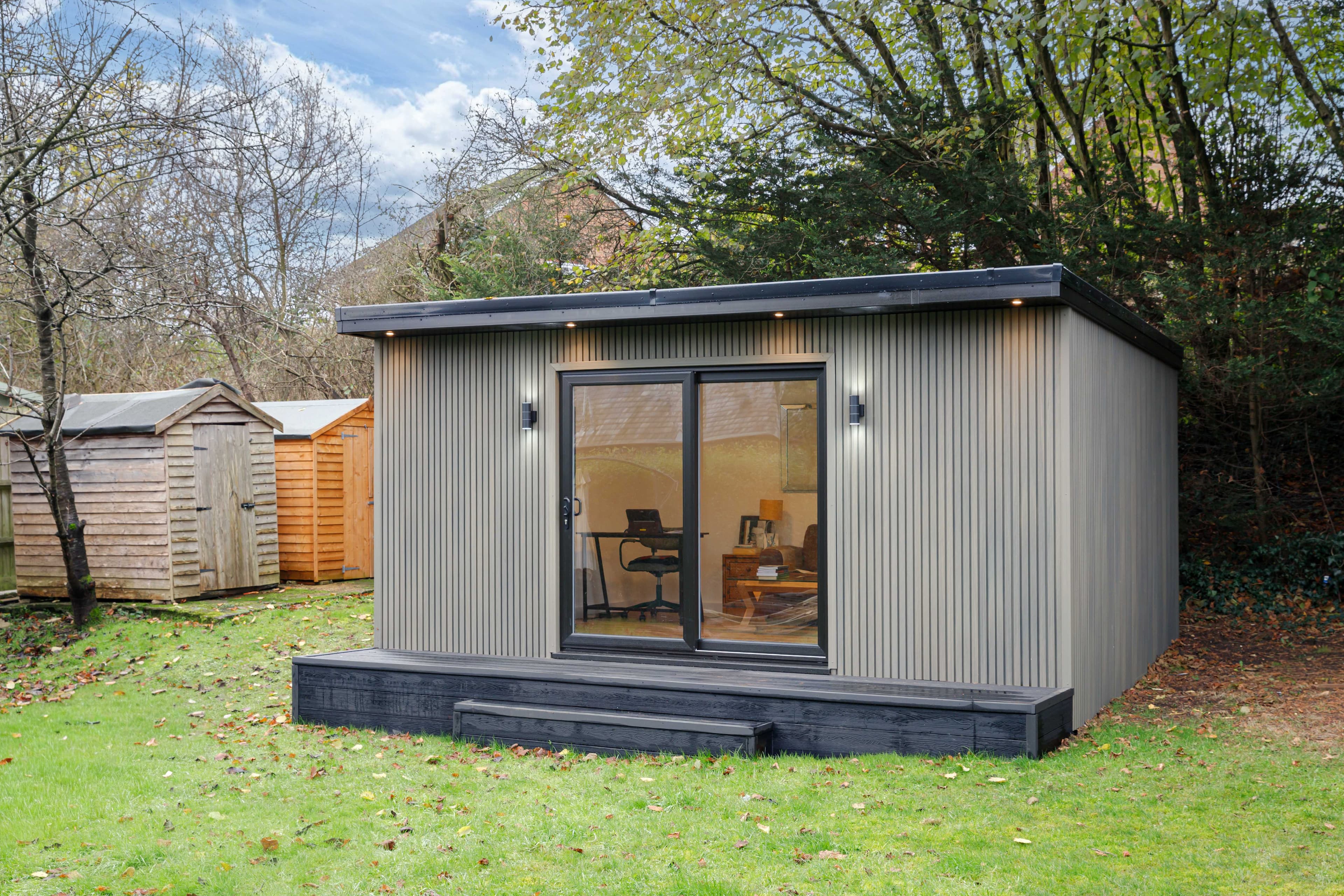 Grey slatted-clad garden office on an autumn lawn in Bedfordshire