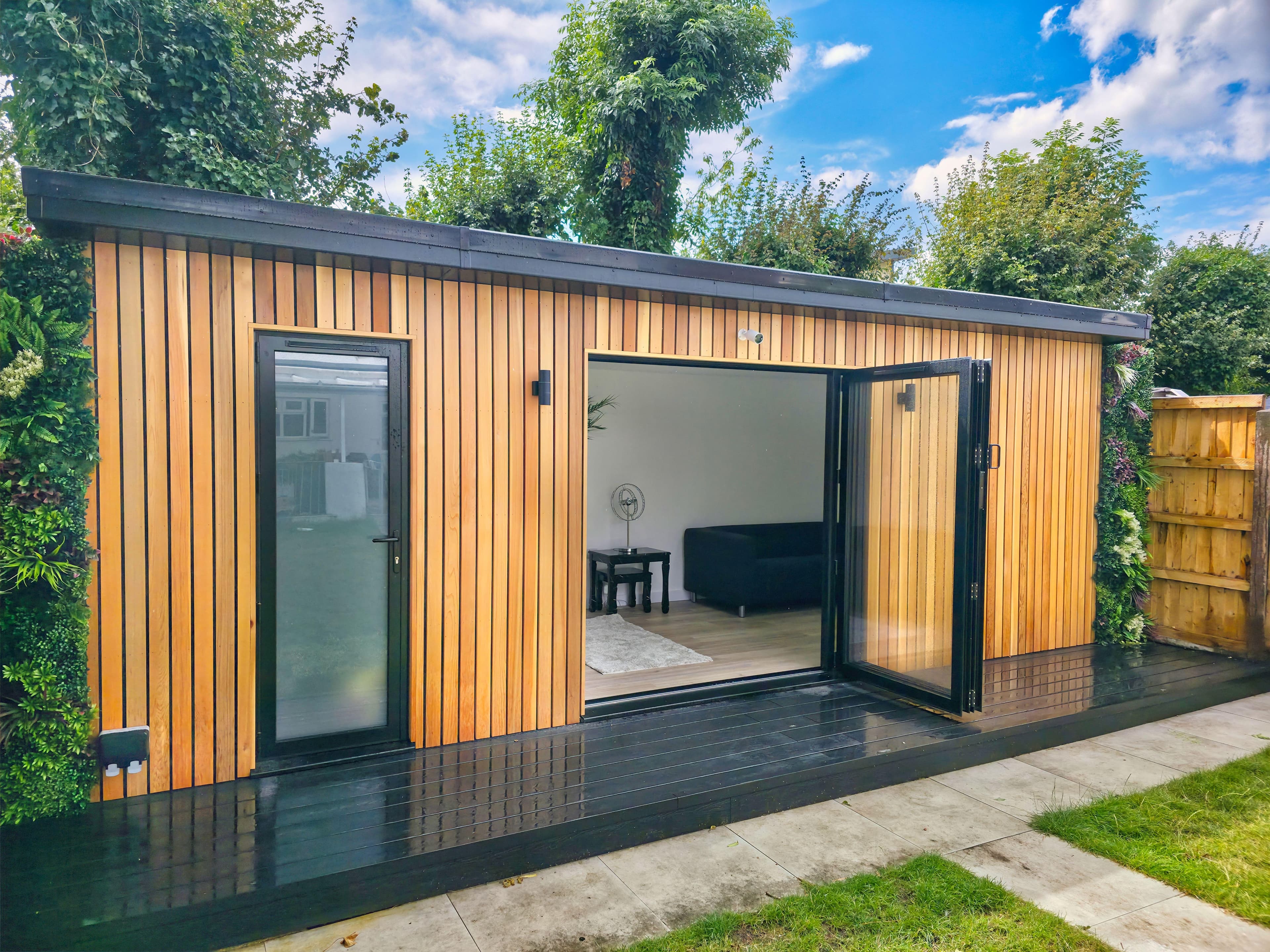 Cedar-clad garden room in Bedfordshire with open bifold doors onto a black deck, framed by a living green wall