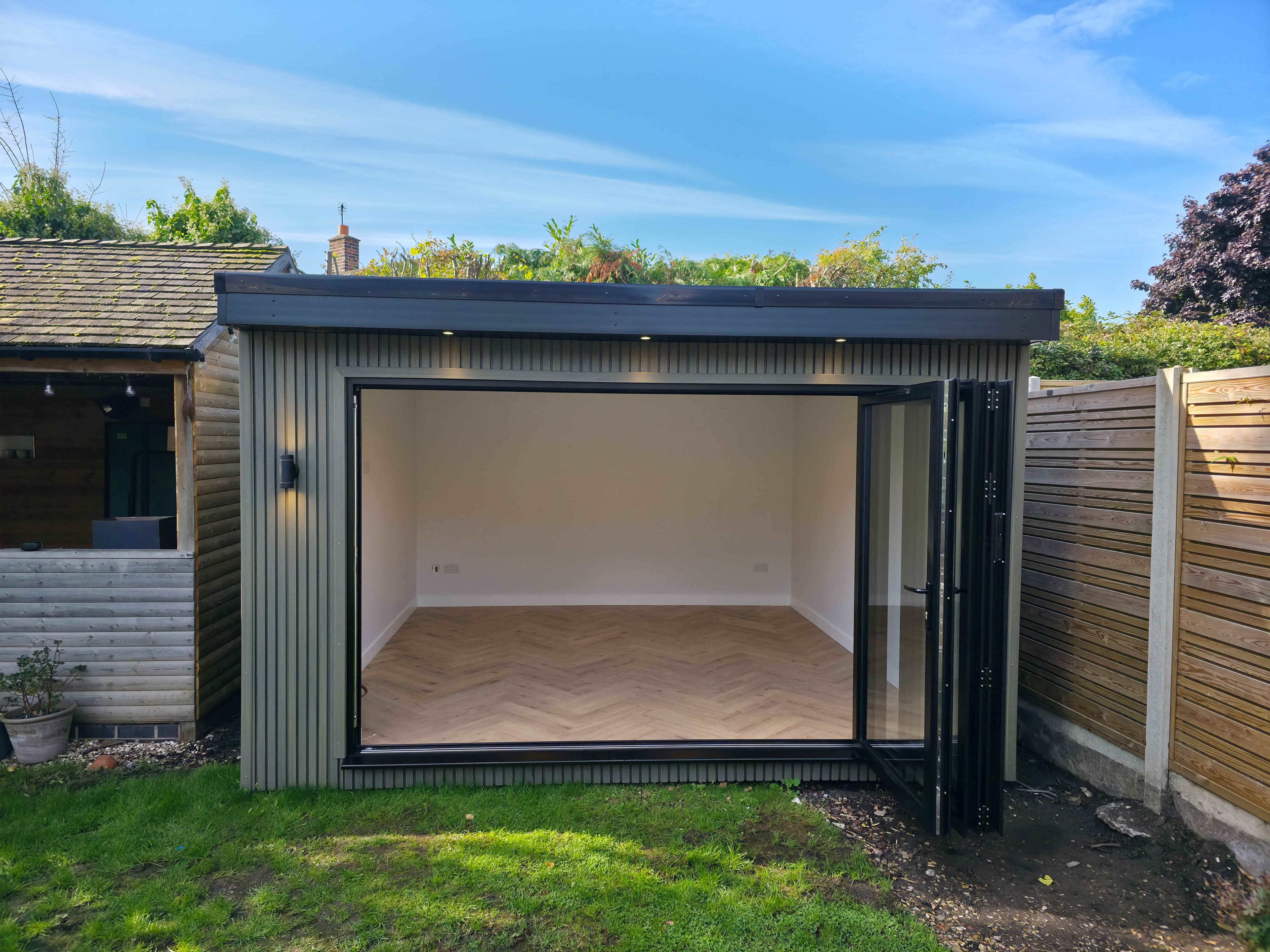 Greige garden room in Bedfordshire with bifold doors folded fully open onto a bright interior with herringbone flooring