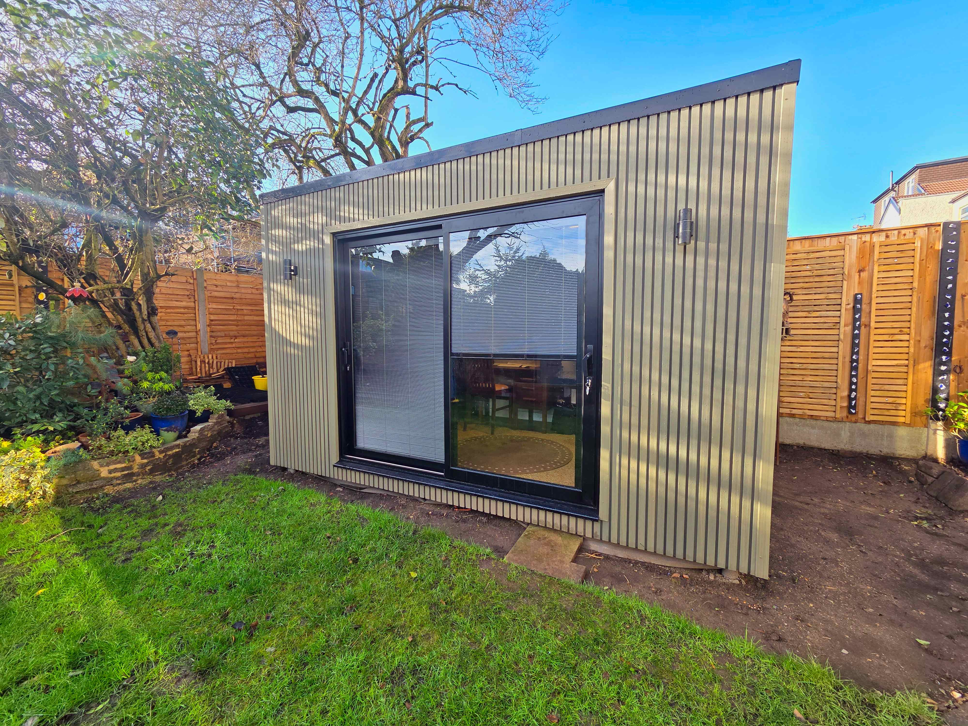 Greige-clad garden room in Bedfordshire with black-framed sliding doors and integral blinds set into the glazing