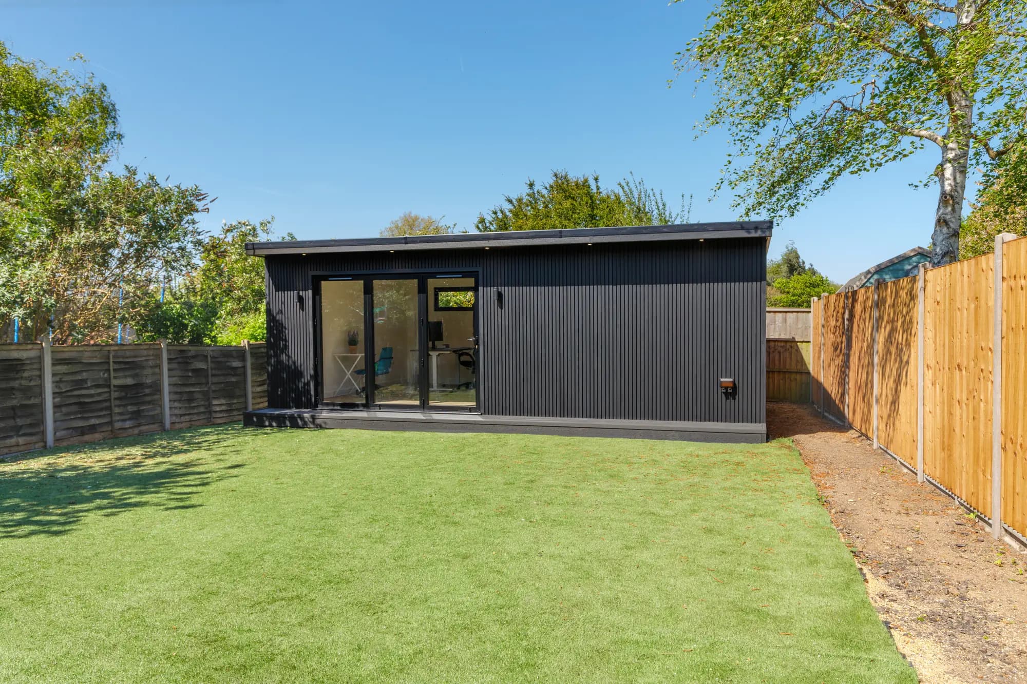 Black-clad garden room with glazed doors in a landscaped garden